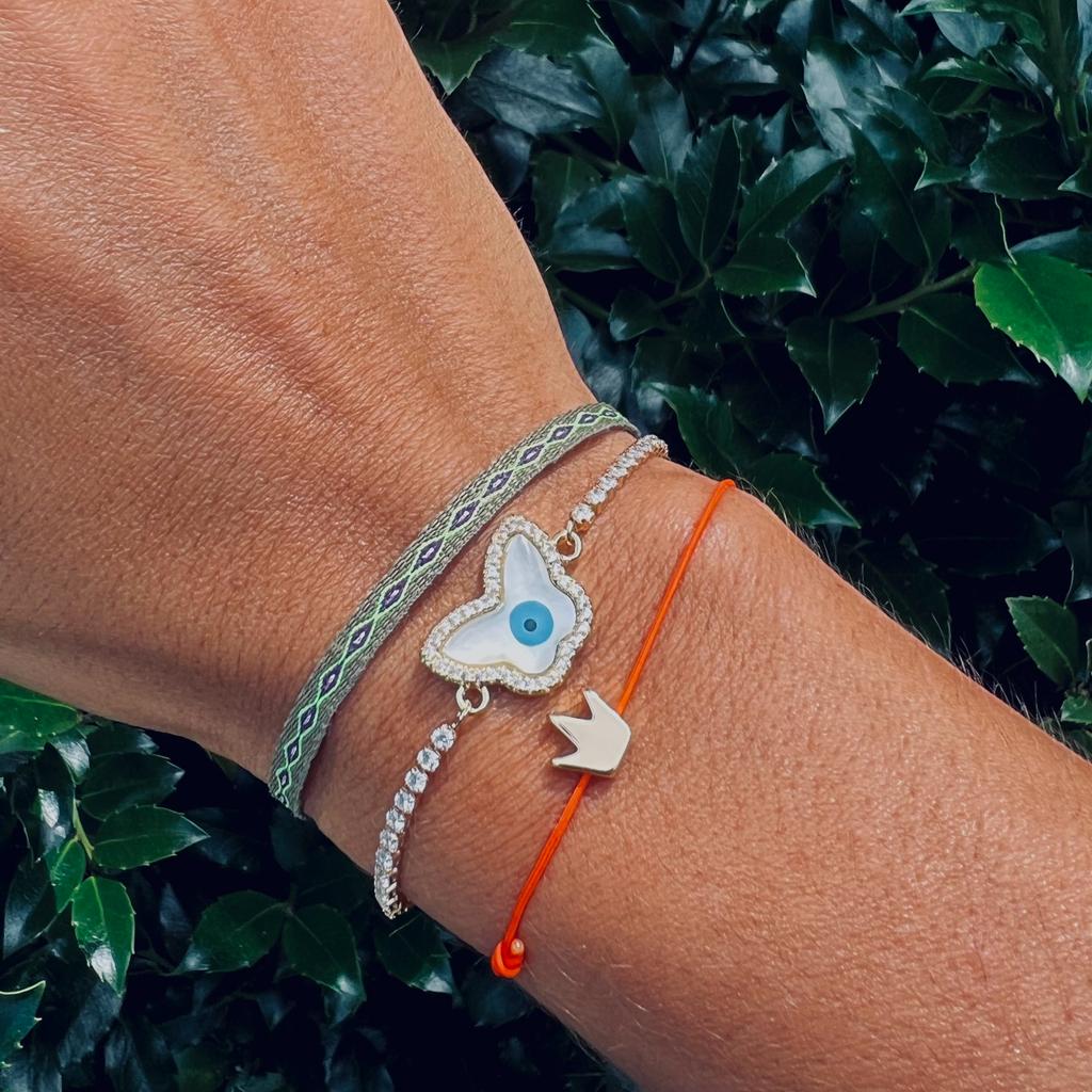 Close-up of a wrist wearing multiple bracelets with decorative charms against a green leafy background
