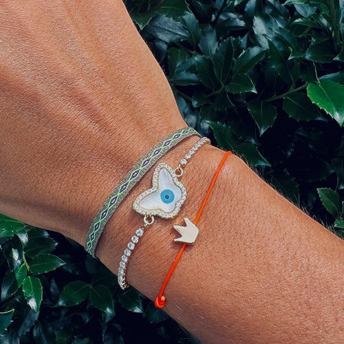 Close-up of a wrist wearing multiple bracelets with decorative charms against a green leafy background